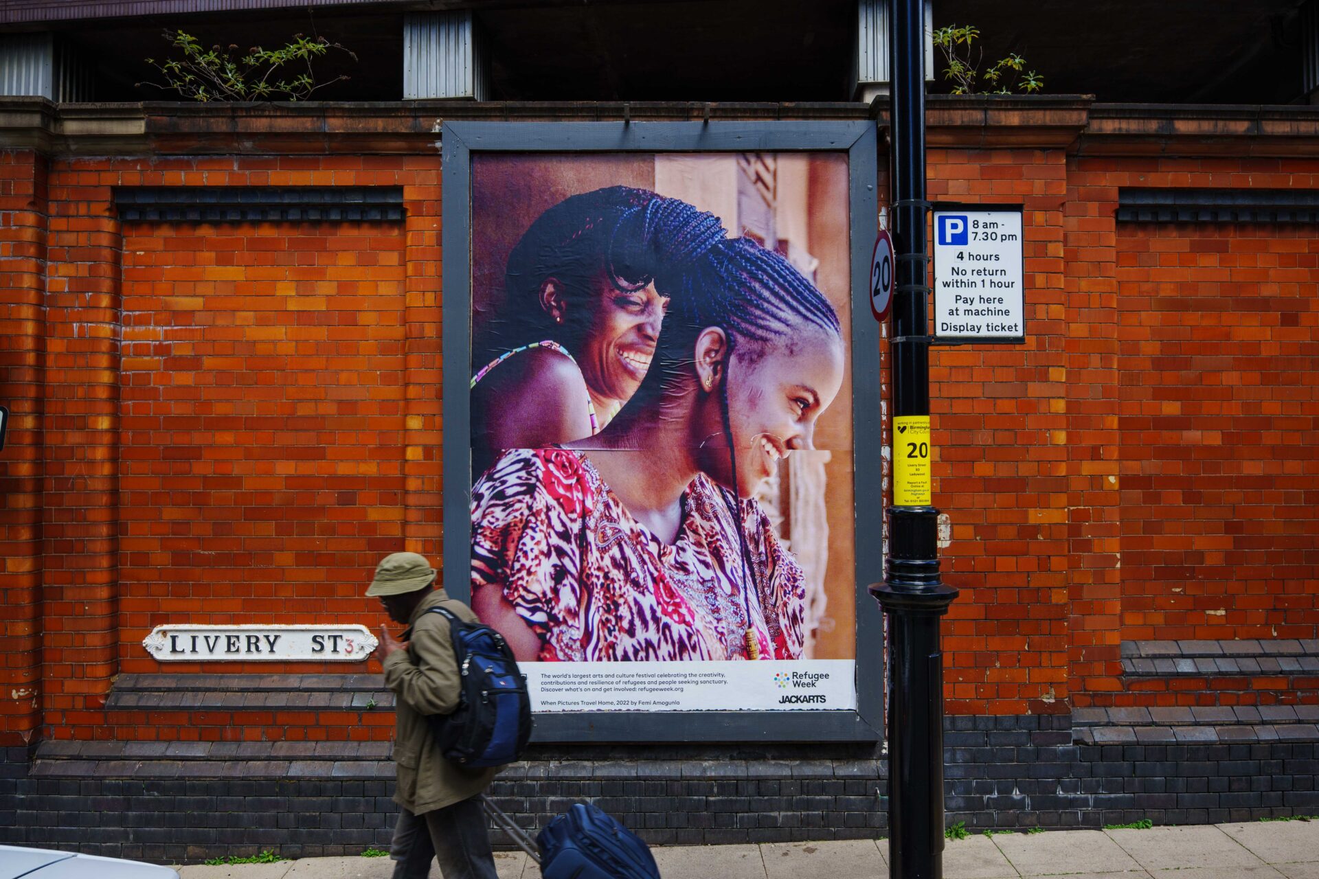A man walks past a large billboard in the street featuring two women of Nigerian heritage laughing together