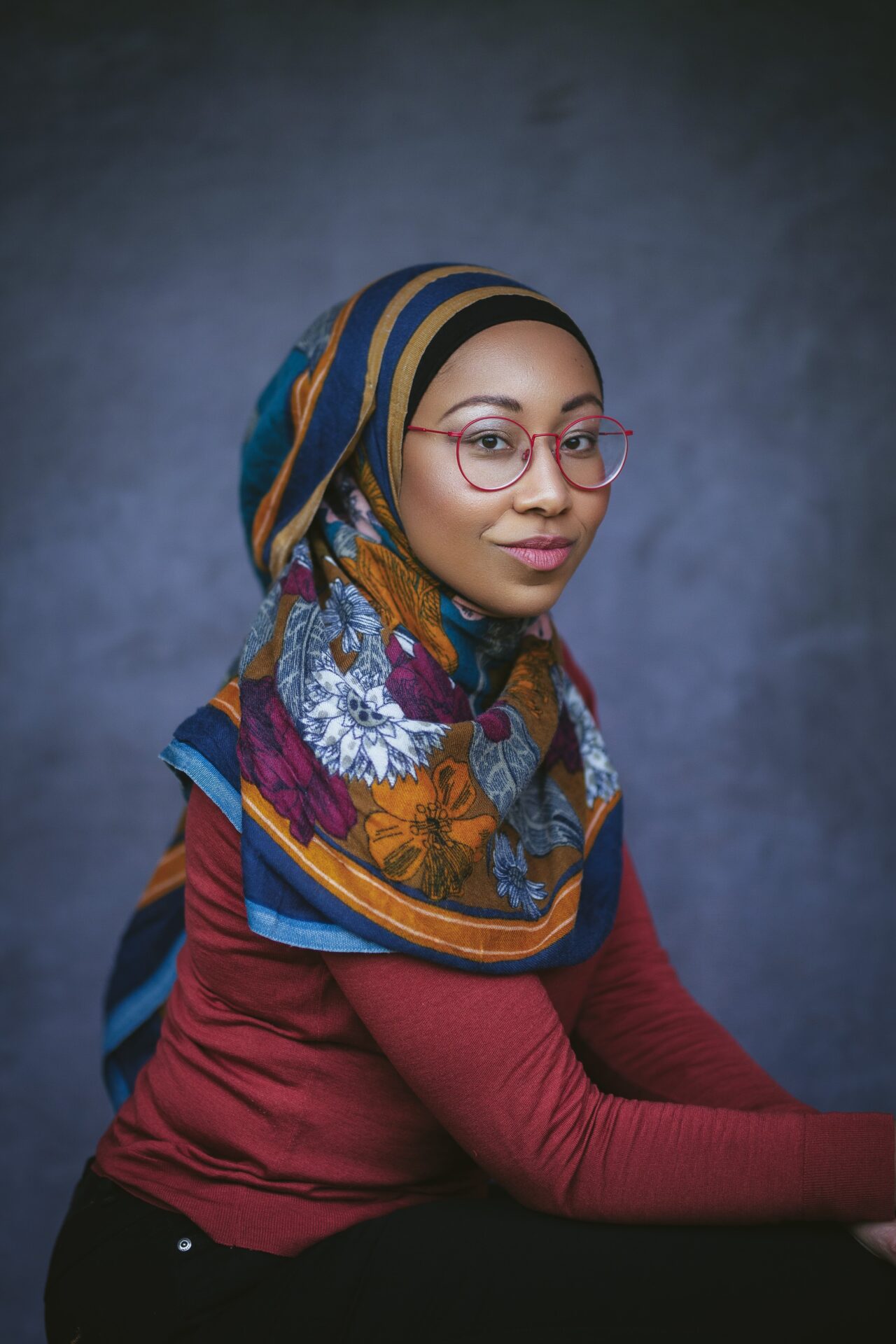 Headshot of a woman wearing glasses, a colourful headscarf and a red top.