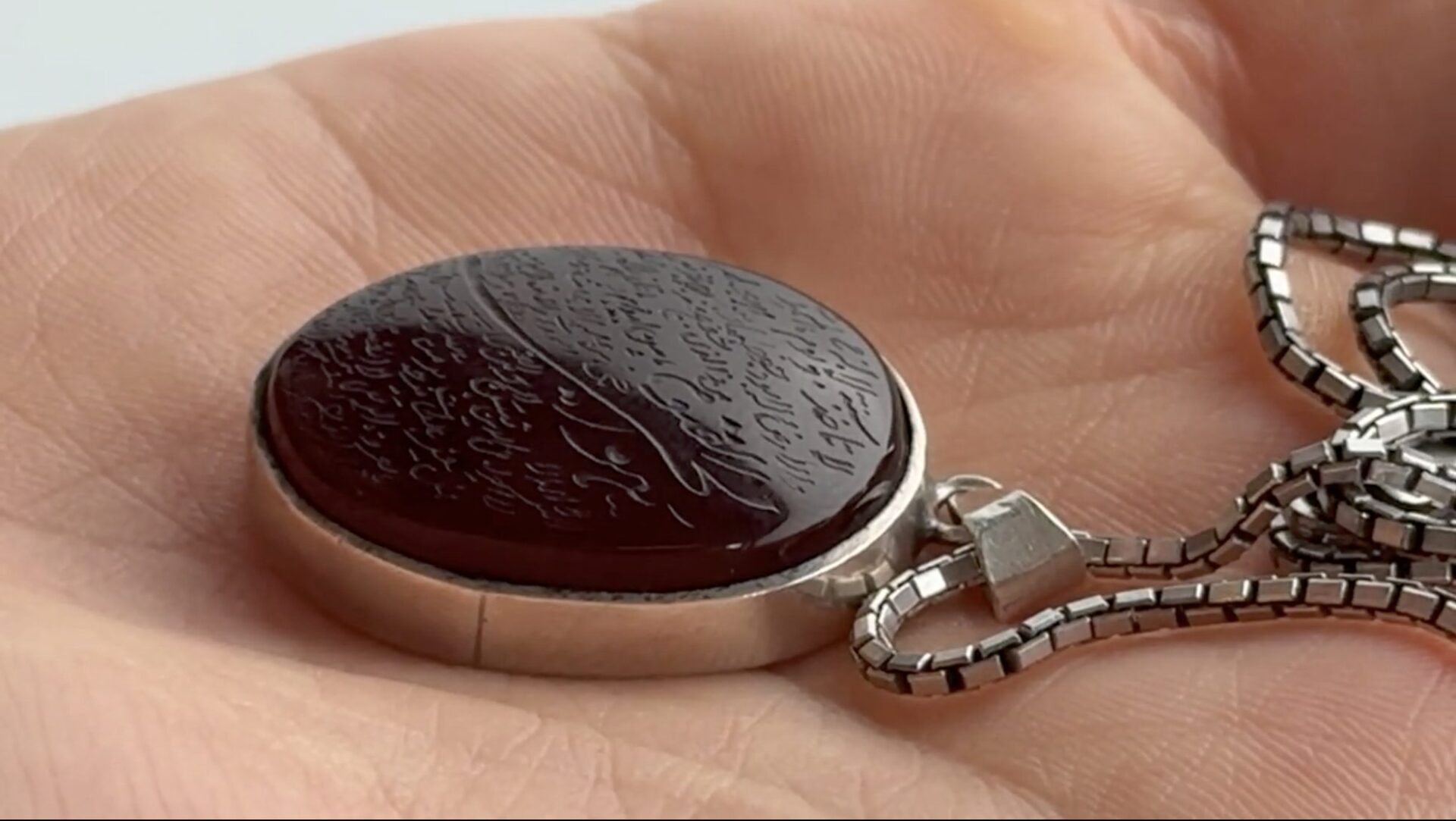A hand holding a necklace with a large pendant with quranic verse inscribed on it