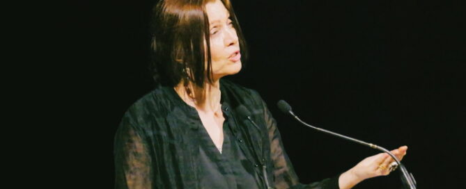 A woman is gesturing as she speaks at a lecturn