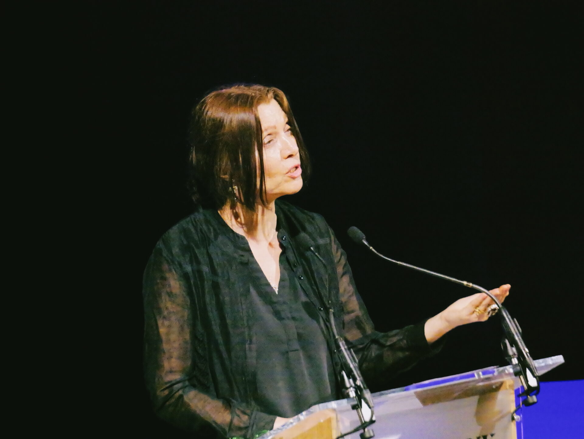 A woman is gesturing as she speaks at a lecturn