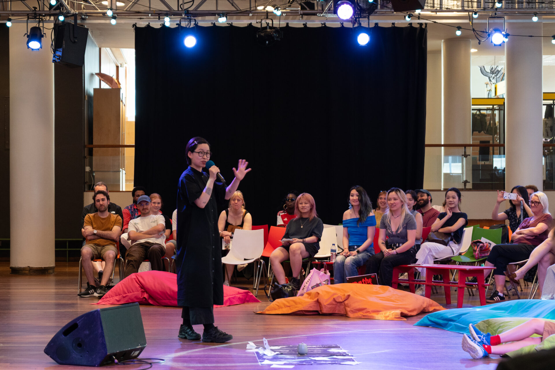An artist speaks into a mic in front of a group of seated people who are smiling